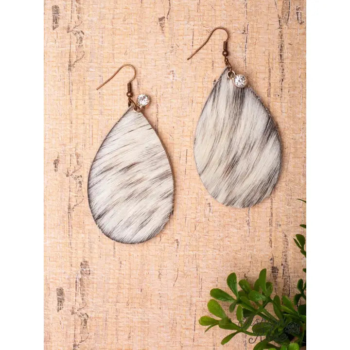 Teardrop-shaped earrings on a textured beige surface with a plant in the corner.