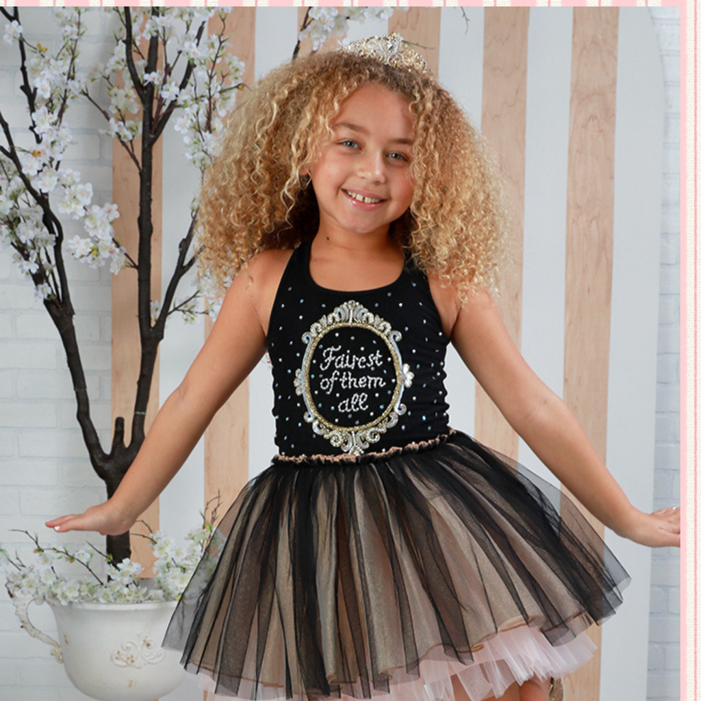 Young girl in a black dress with floral design and text, standing in front of a decorative background.