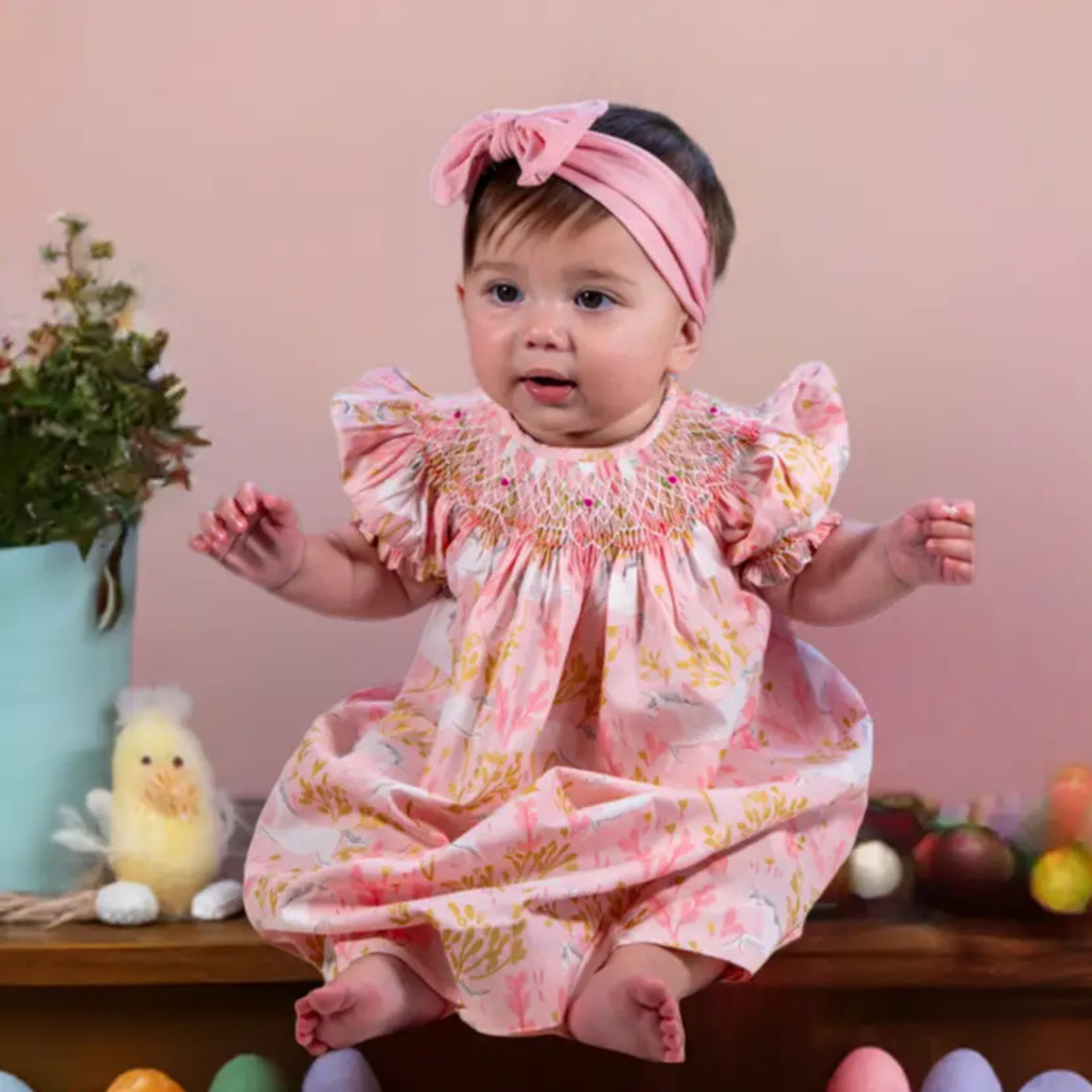 Baby in a floral dress with a pink headband against a pink background