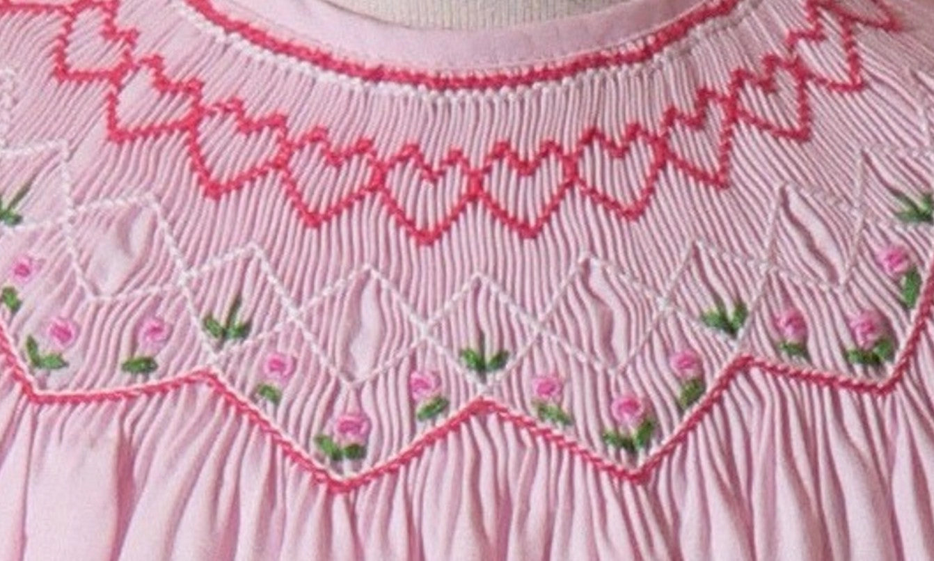 Close-up of a pink garment with intricate smocking and floral embroidery