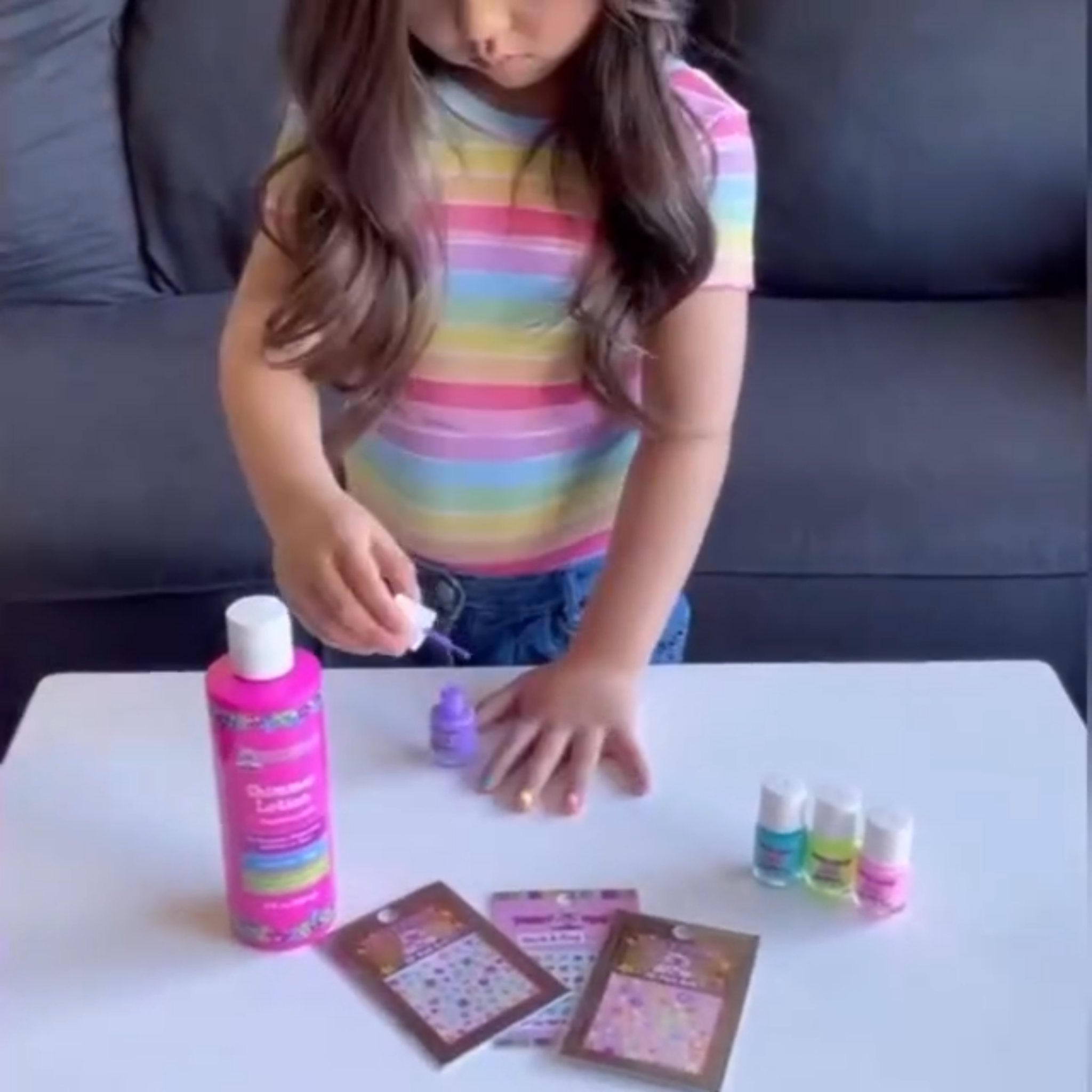 Child with colorful striped shirt interacting with small nail polish bottles and sticker cards on a table.